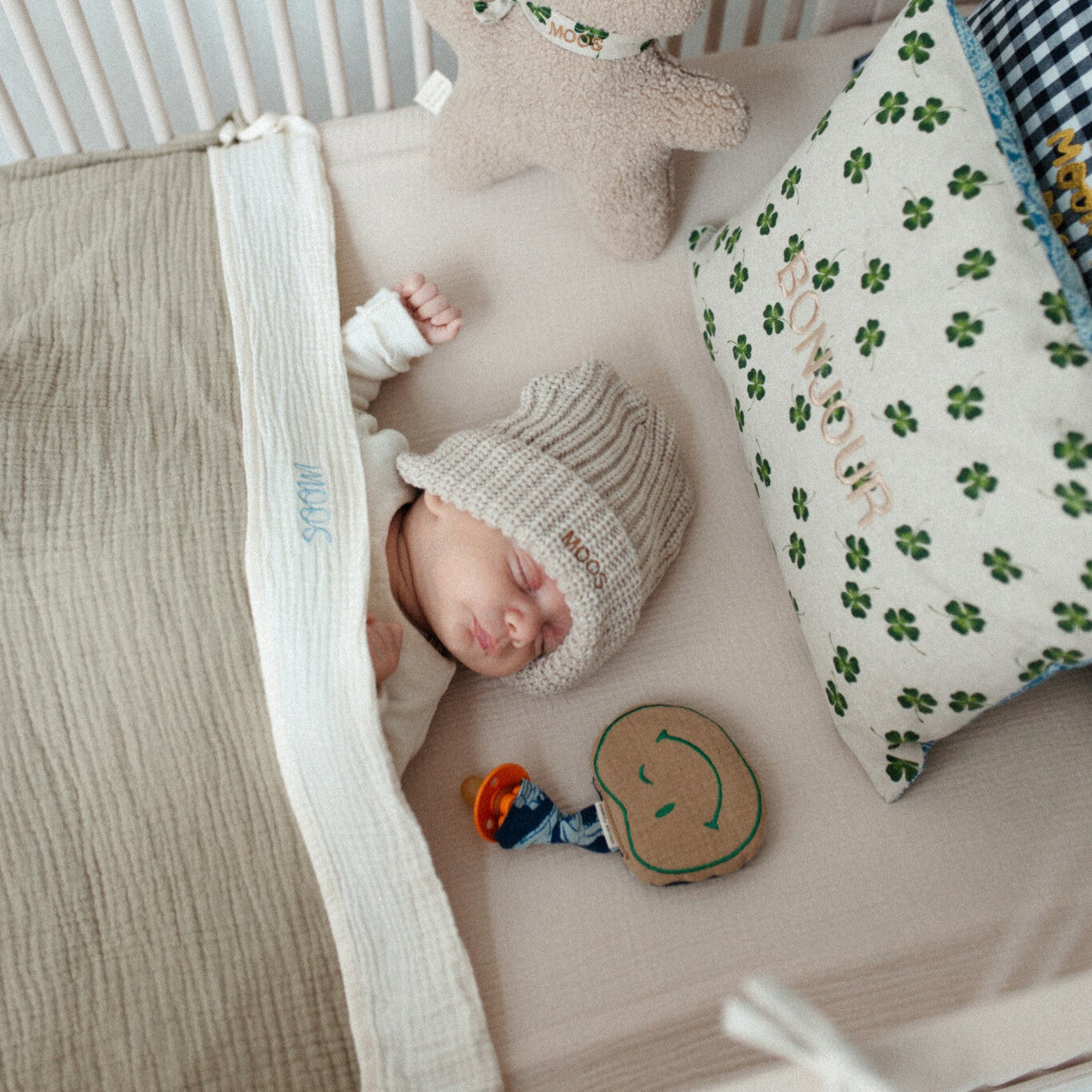 baby ligt in ledikant met kussen met tekst, knuffel, speen met speenknuffel.