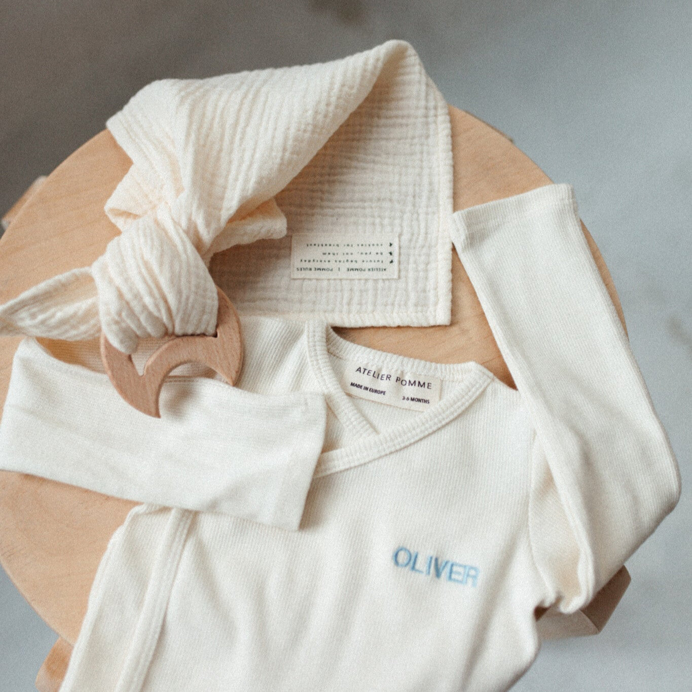 bijtring met speenkoord en romper met gepersonaliseerde tekst liggend op een kruk