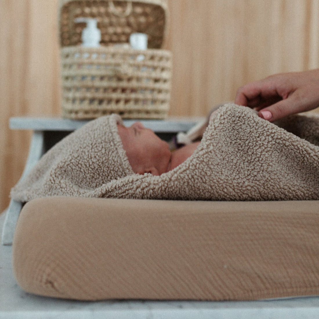 baby ligt in teddy deken met capuchon op aankleedkussen 